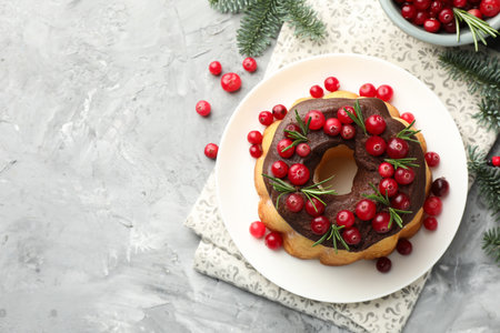 Delicious Christmas cake with chocolate glaze, cranberries, rosemary and fir tree branches on gray textured table, flat lay. Space for textの写真素材