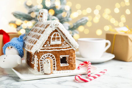 Gingerbread house and Christmas decor on white table against blurred lightsの写真素材