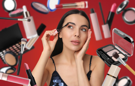 Beautiful makeup artist with mascara on red background. Decorative cosmetics falling around herの写真素材