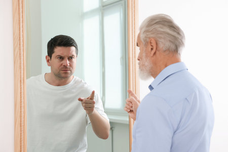 Senior man seeing himself in mirror. Concept of personality, past and future, flow of time, ageの写真素材