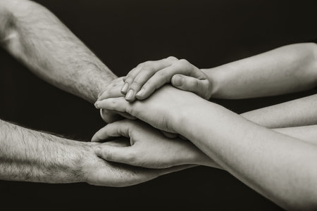 Young people putting their hands together on dark background, closeup. Color toning