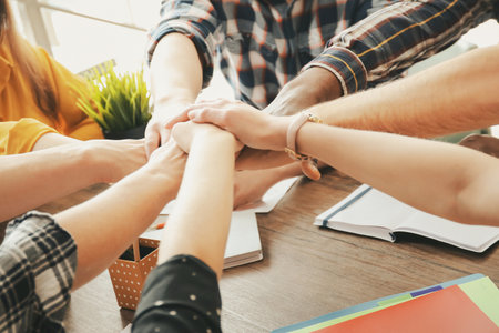 People putting hands together at table, closeup. Unity concept