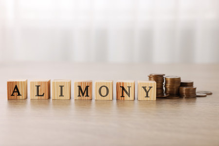 Alimony word made of cubes with letters and stacked coins on wooden tableの写真素材