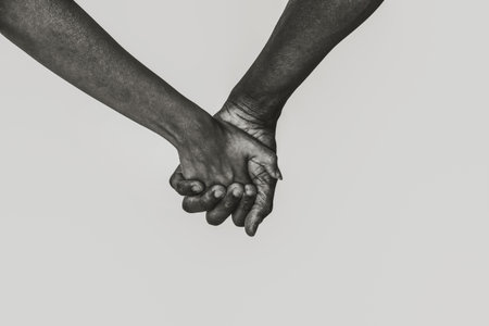 Woman and African American man holding hands on white background, closeup. Black and white toning