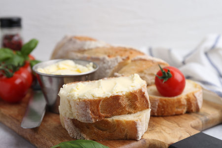 Cut baguette with butter, basil, tomatoes and knife on light table, closeupの写真素材