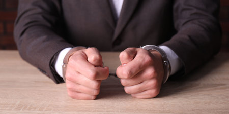 Man in handcuffs at wooden desk indoors, closeupの写真素材