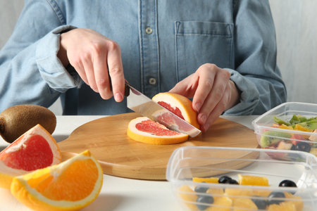 Making fruit salad. Woman cutting grapefruit at white table, closeupの写真素材