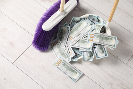 Sweeping dollar banknotes with broom into dustpan on light wooden floor, closeupの写真素材