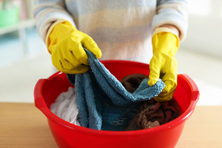 Woman washing towels in plastic basin at table indoors, closeupの写真素材