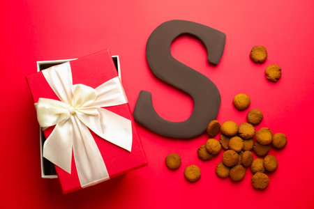 Saint Nicholas (Sinterklaas) day. Chocolate letter S, kruidnoten cookies and gift box on red background, flat layの写真素材