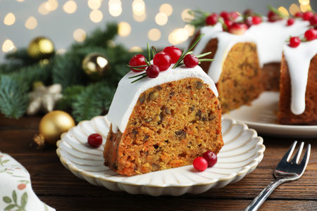Slice of tasty Christmas cake with cranberries served on wooden table against blurred lights, closeupの写真素材