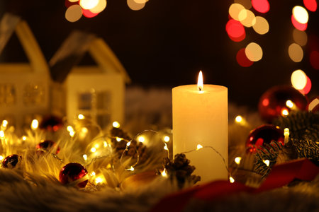 Burning candle, fir tree branches, baubles, cones and festive lights on faux fur against black background with blurred lights, closeup. Bokeh effectの写真素材