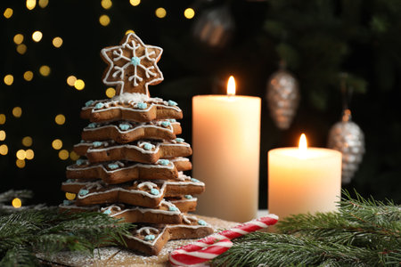 Christmas tree made of gingerbread cookies, fir branches, candy cane and burning candles against black background with blurred lightsの写真素材