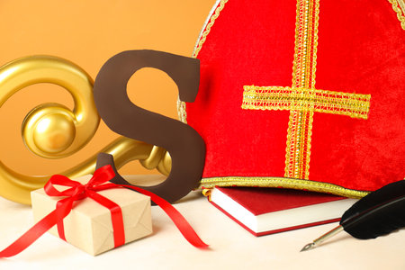 Sinterklaas (Saint Nicholas) Day. Chocolate letter S, mitre, crosier, gift, notebook and feather on white table, closeupの写真素材