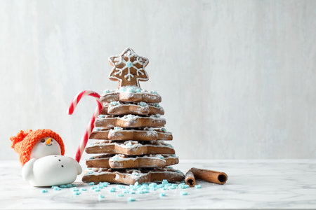 Delicious Christmas cookie tree with sprinkles, icing and decorative snowman on light marble table, closeup. Space for textの写真素材