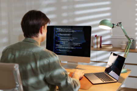 Programmer working on computer at table in office, back viewの写真素材