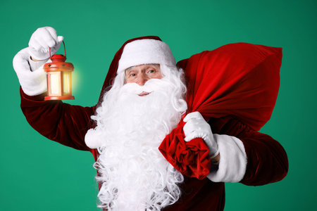 Santa Claus with red bag of Christmas gifts and lantern on green backgroundの写真素材
