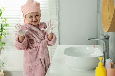 Happy girl in bathrobe with soapy hands near sink at homeの写真素材
