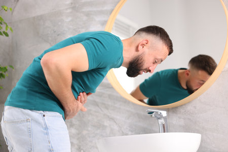 Man suffering from stomach ache and nausea over sink in bathroomの写真素材
