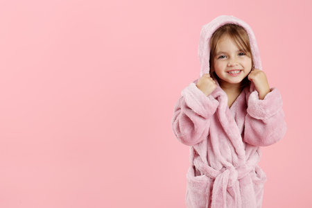 Cute girl in bathrobe on pink background. Space for textの写真素材
