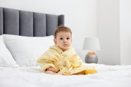 Cute baby in bathrobe on bed at home. Space for textの写真素材