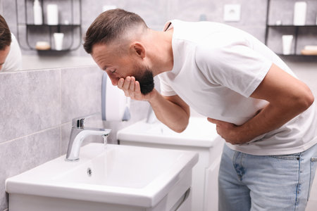 Man suffering from stomach ache and nausea over sink in bathroomの写真素材