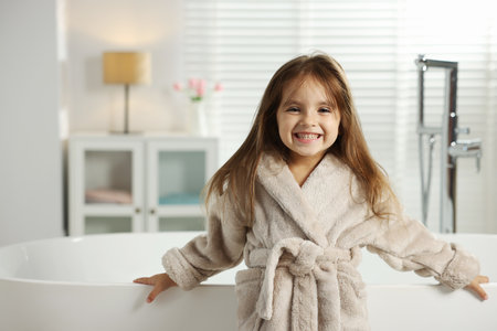 Happy girl in bathrobe near bathtub at home. Space for textの写真素材