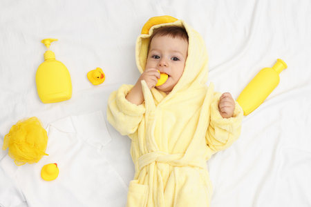 Cute baby in bathrobe and bathroom accessories on bed, top viewの写真素材