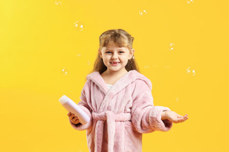 Happy girl in bathrobe with shampoo and bubbles on yellow backgroundの写真素材