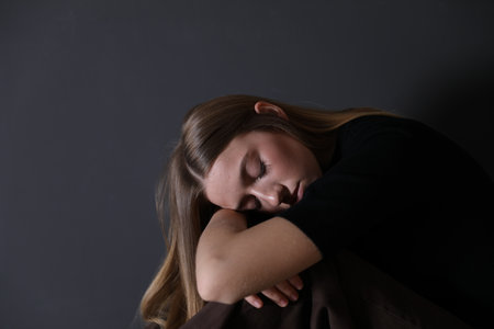 Depressed teenage girl near black wall indoors, space for textの写真素材