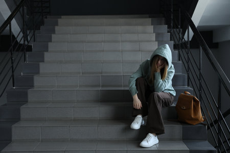 Depressed teenage girl and backpack on stairs indoors, space for textの写真素材