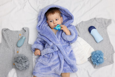Cute baby in bathrobe, clothes and bathroom accessories on bed, top viewの写真素材