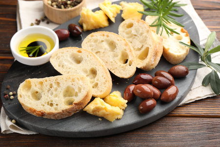 Pieces of fresh ciabatta, butter, olives, cheese, rosemary and peppercorns on wooden table, closeup