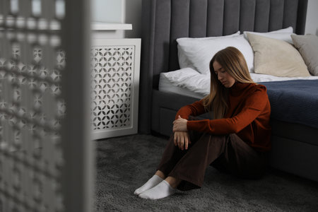 Depressed teenage girl near bed at homeの写真素材
