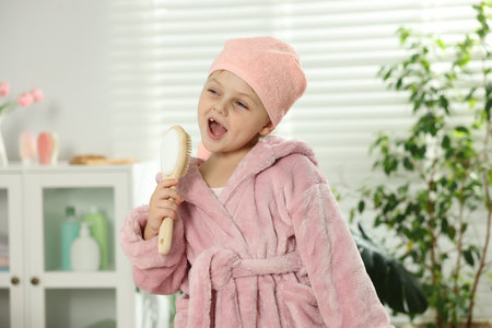 Little girl in bathrobe with brush as microphone singing at bathroomの写真素材