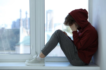 Depressed teenage boy near window at homeの写真素材