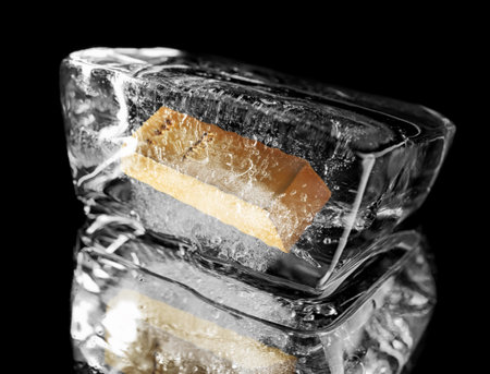 Gold bar in ice cube on black background.の写真素材