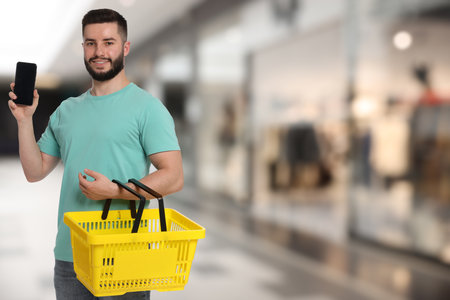 Man holding empty shopping basket and mobile phone at supermarketの写真素材