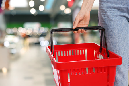 Customer holding empty shopping basket at supermarket, closeup