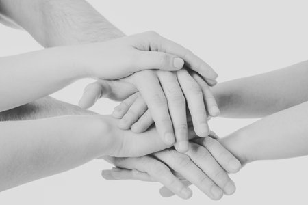 Young people putting their hands together on white background, closeup. Black and white toning