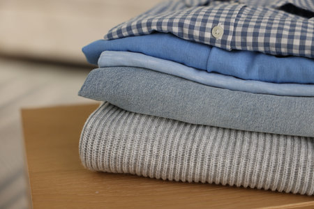 Stack of clean clothes on wooden table indoors, closeup. Space for text