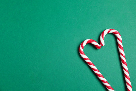 Heart made of candy canes on green background, top view with space for text. Christmas treatの写真素材