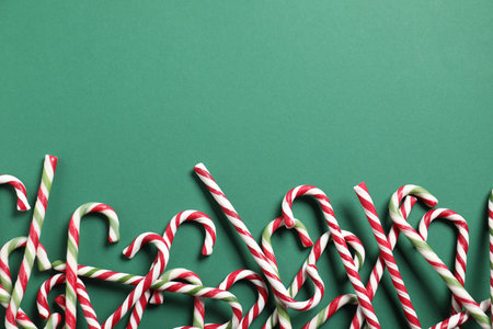 Tasty candy canes on green background, flat lay with space for text. Christmas treatの写真素材