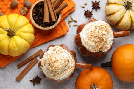 Tasty pumpkin latte with whipped cream in cups, spices and ingredients on light gray table, flat layの写真素材