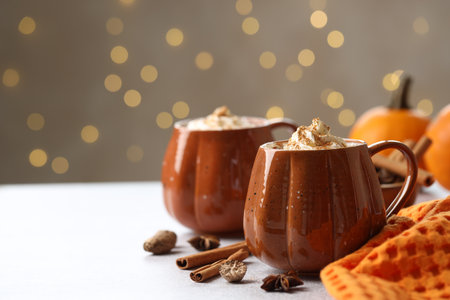 Tasty pumpkin latte with whipped cream in cups, spices and ingredients on light gray table against blurred lights, space for text. Bokeh effectの写真素材