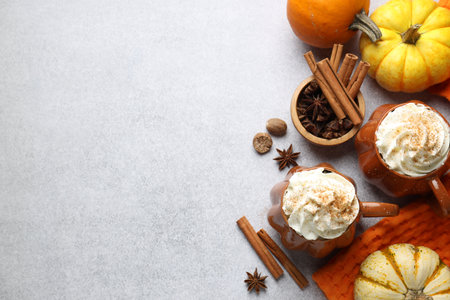 Tasty pumpkin latte with whipped cream in cups, spices and ingredients on light gray table, flat lay. Space for textの写真素材