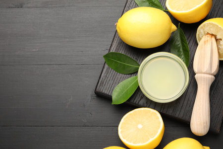 Fresh lemon juice, fruits and squeezer on black wooden table, flat lay. Space for textの写真素材