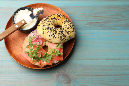 Delicious bagel with salmon, cream cheese, onion and arugula on light blue wooden table, top view. Space for textの写真素材