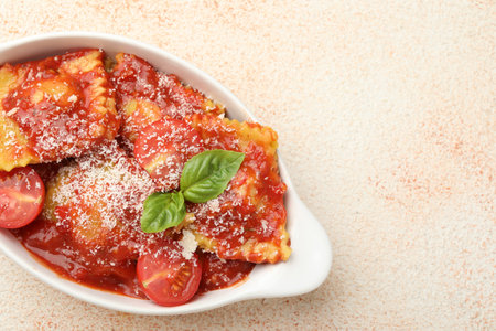 Delicious ravioli with tomato sauce, cheese and basil in baking dish on light textured table, top view. Space for textの写真素材