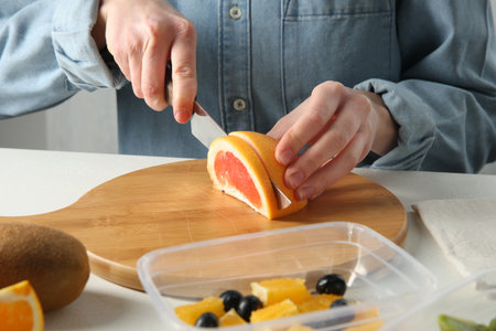 Making fruit salad. Woman cutting grapefruit at white table, closeupの写真素材